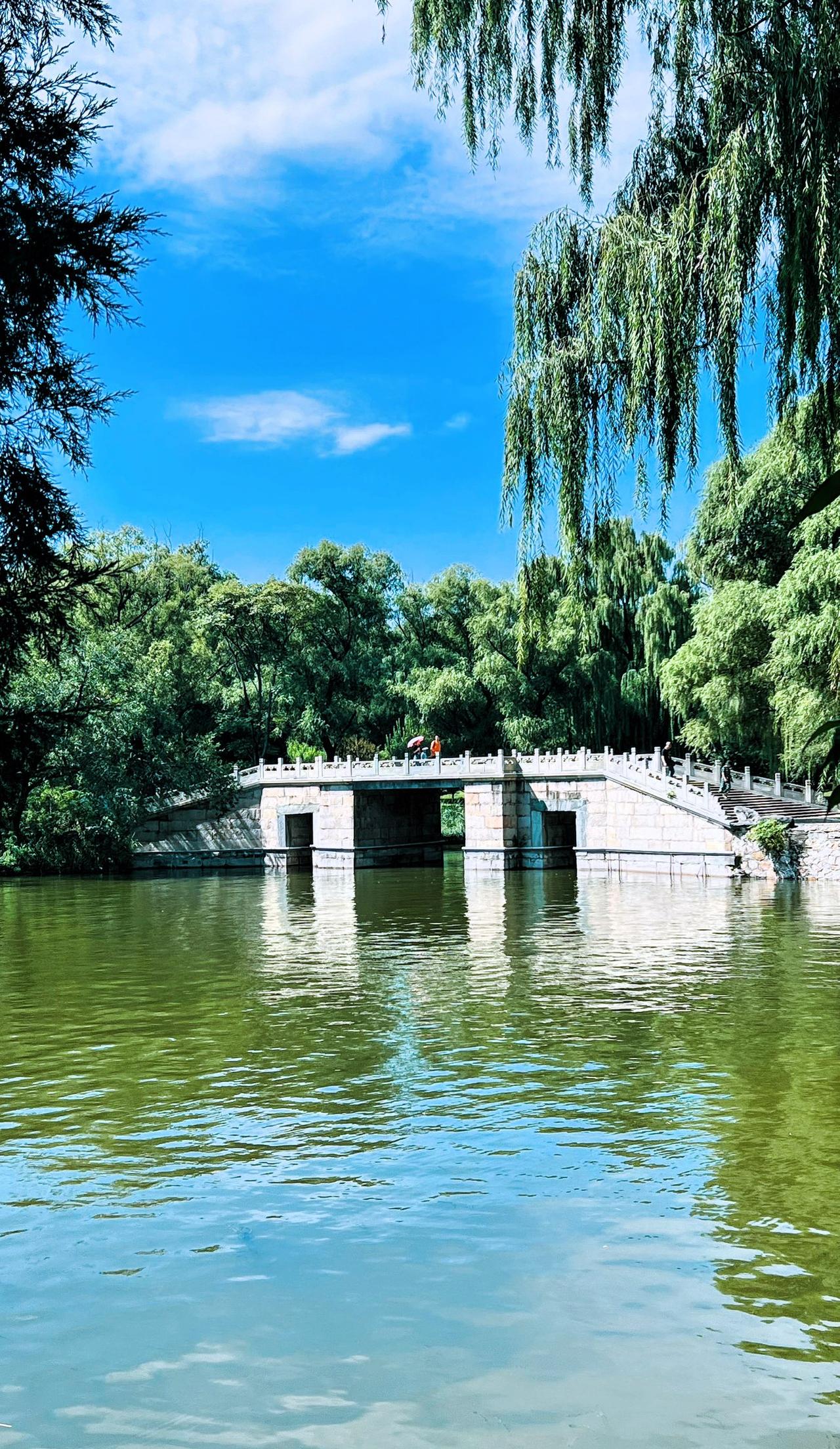 分享一张风景照片：蓝天白云，静谧湖畔，湖水碧绿，古桥横卧，绿树成荫，风景这边独好