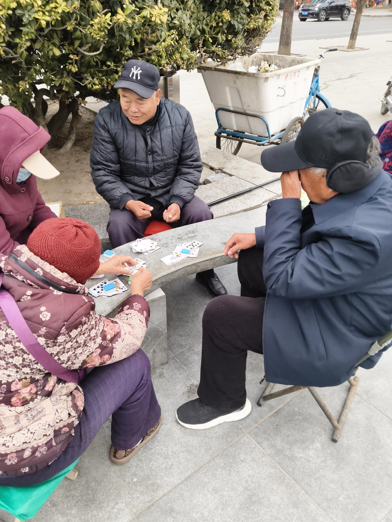 暖阳透过枝叶，在石桌上洒下斑驳光影。几位老人围坐，指尖翻飞的扑克牌，是他们专属的