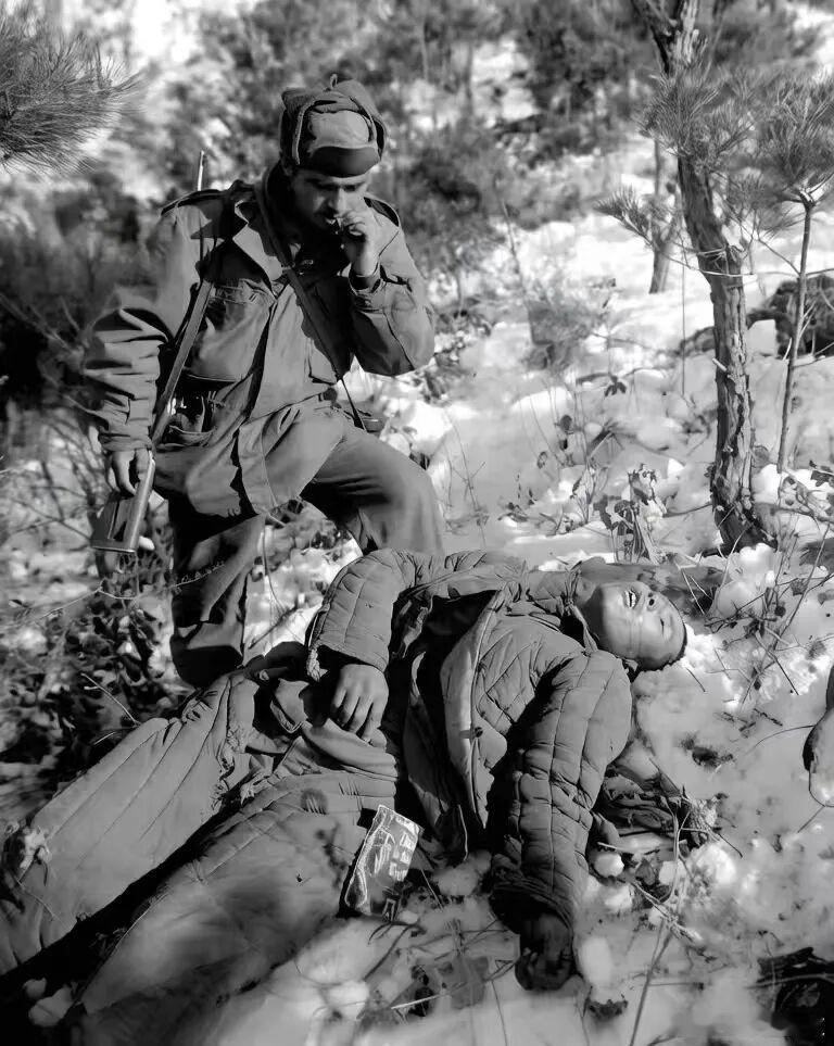 1951年这个美军在抽烟在他的脚边有位志愿军战士他倒在露天的雪地里口鼻处还有鲜血