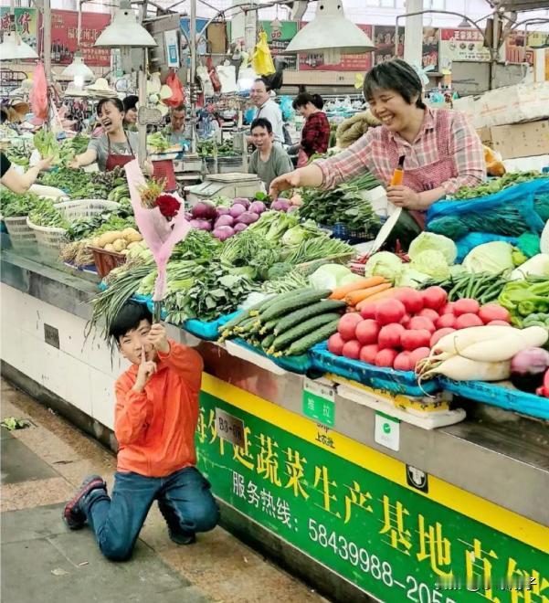 一个孩子跪在摊位前面，手里还拿着一捆东西，当他举起来的时候，赢得了众多人的夸赞。