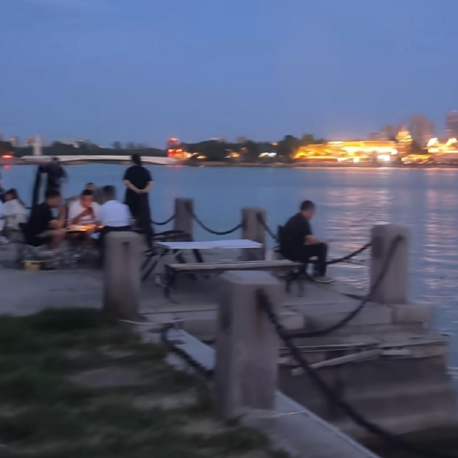 这是聊城东昌湖风景区的夏日黄昏景象，湖面波光粼粼，远处摩天轮与古城灯光交相辉映，