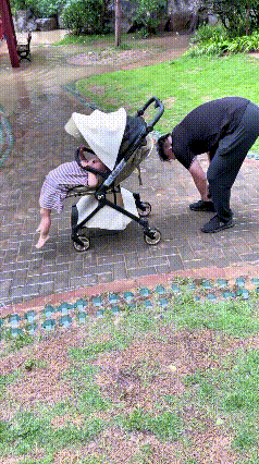 恁瞅瞅这爹，心咋恁大嘞！刚下完雨，他推着娃想趟水过去，还特意停下来弯腰挽裤脚，结