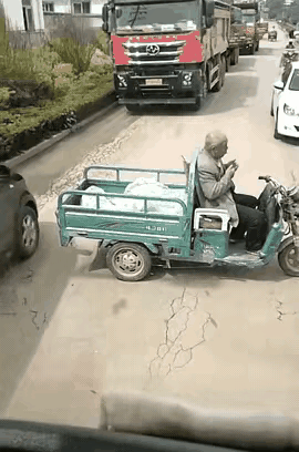 这哪是大爷心大啊，这路被大货车压得坑坑洼洼，连个靠边的地方都没。他也只能在路中间