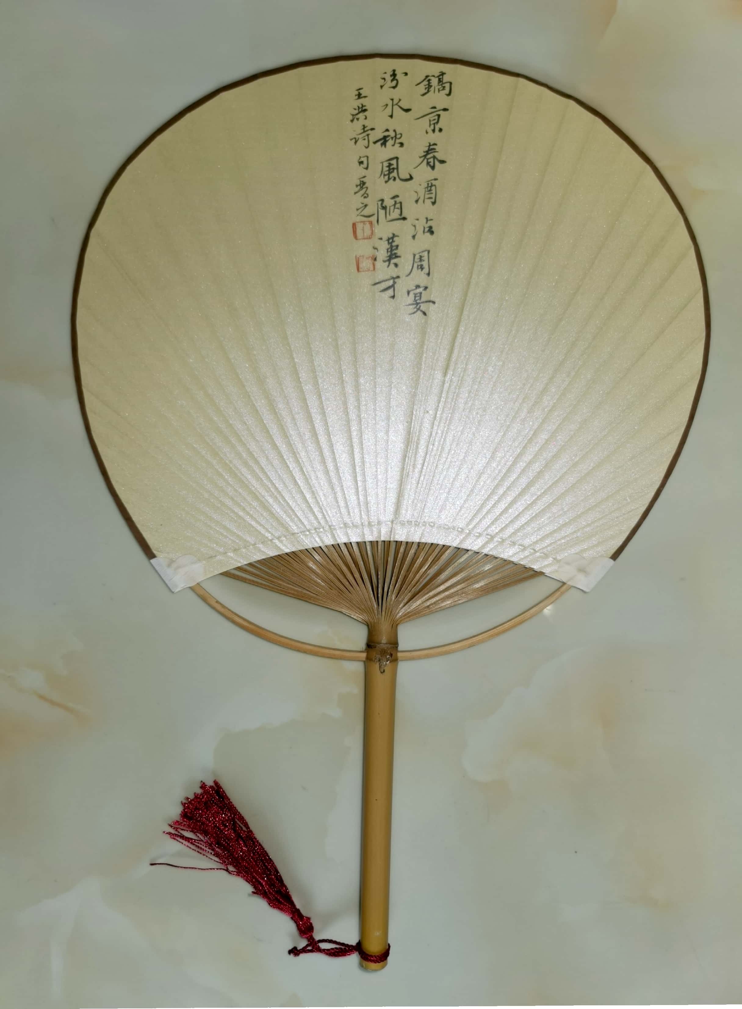 《素扇墨痕，竹骨清韵》素面团扇配以浅淡竹柄，红穗垂落，扇面仅顶端一行墨字“镐京春