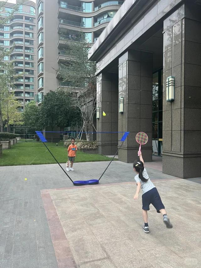 现在的小孩了不得，小区空地几个小学生搭了个简易球网打羽毛球，一位家长在旁指导：“