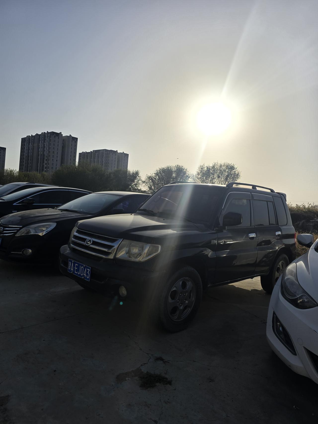 在一个露天停车场里，一台黑色的小车安安静静地停在几台家用轿车中间，在傍晚阳光的斜