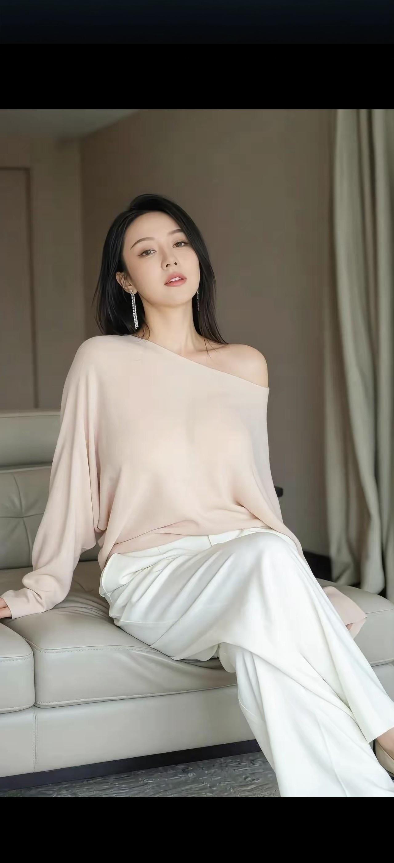 她坐在沙发上，穿着粉色上衣和白色裤子。