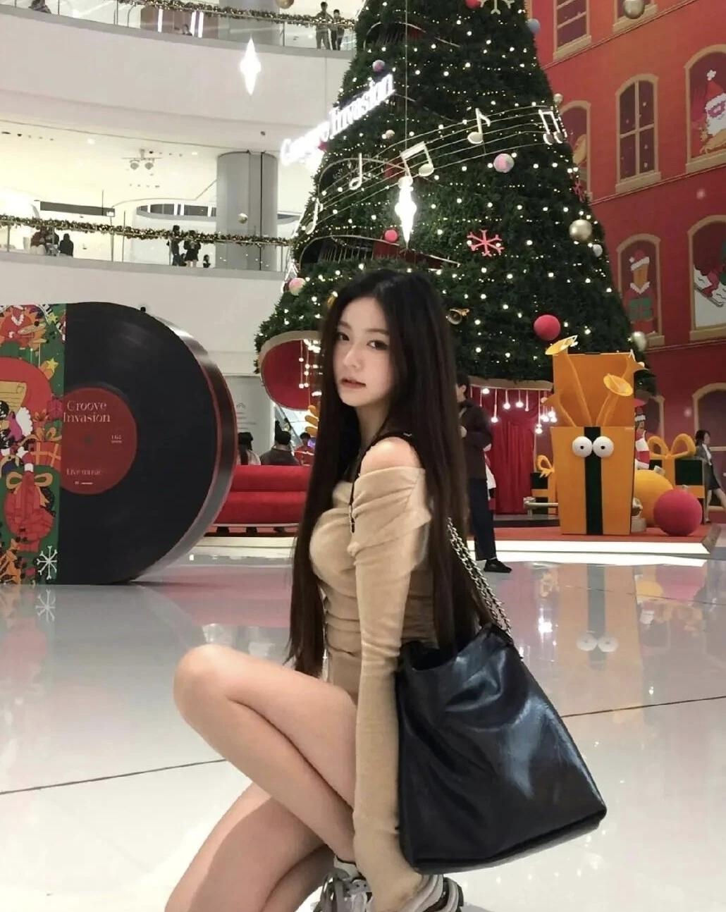 🎄 蹲在满是星光的圣诞树前，浅棕露肩衫配黑包，把商场的圣诞氛围和松弛感都揣进怀