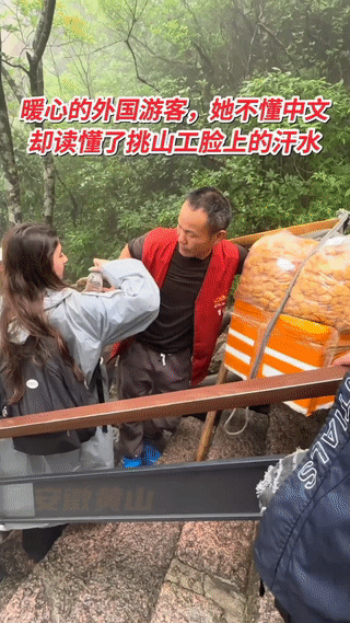 安徽黄山景区。
一对外国情侣在山上看到一位挑山工大叔累的满身大汗，工作很不容易。
