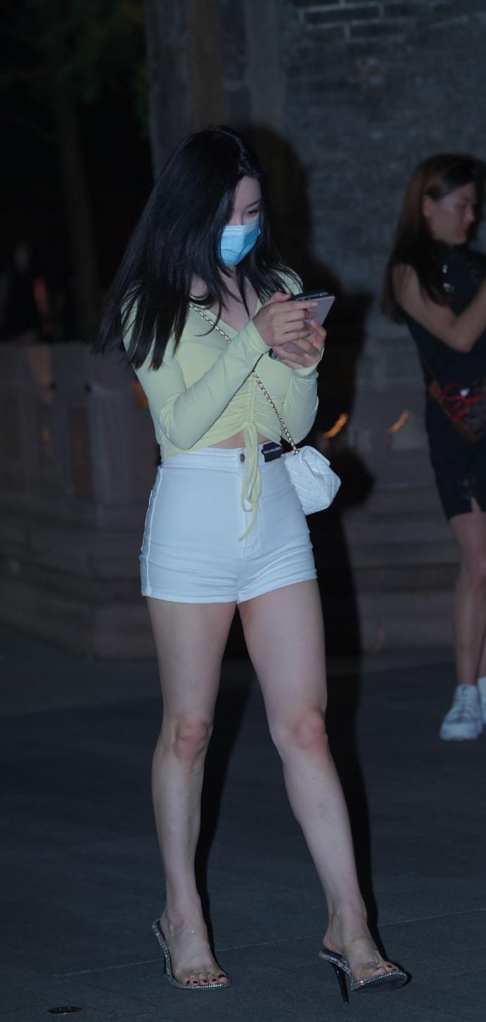 夜色笼罩下的都市街头，她身着一袭清新装扮，宛如一道亮丽的风景线。嫩黄色抽绳上衣，