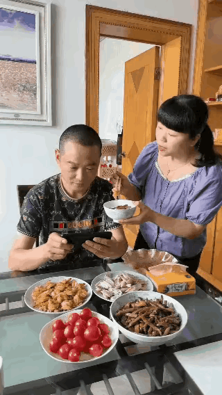 闺蜜来家玩，见到她老婆，给老公做了几个好菜，老公在饭桌前玩着手机，老婆夹了一口菜