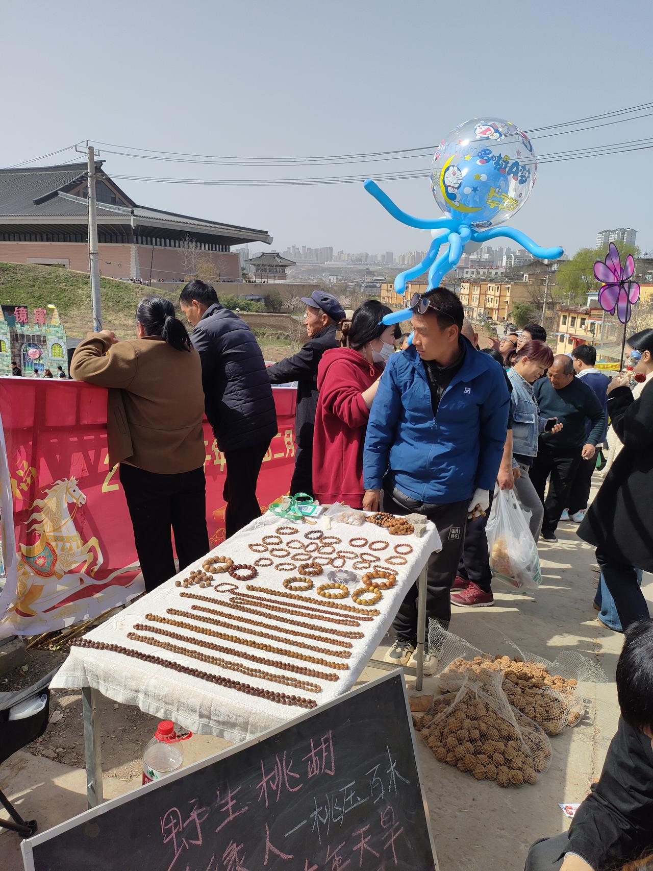 春日集市里，手串与桃核摊前挤满了好奇的人，哆啦A梦气球飘在热闹的人潮之上，老物件