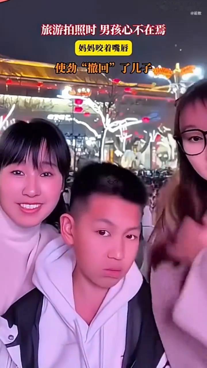 旅游拍照时男孩心不在焉，妈妈咬着嘴唇使劲"撤回"了儿子。
姐姐，妈妈，儿子。