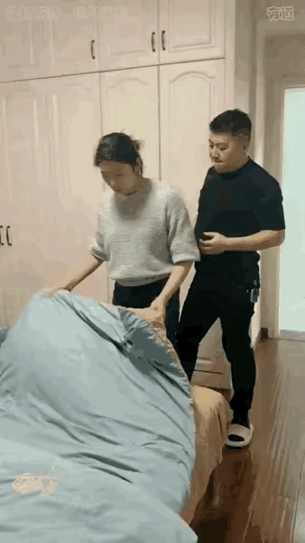 老婆在家整理被子，老公过来抱住了老婆，老婆挣脱他的束缚回手一拳说，你欠揍呀，老公
