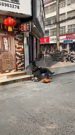 街头拍到一位流浪乞讨的大爷正坐在马路边上晒太阳。
可能看到为了取暖，这位大爷还点