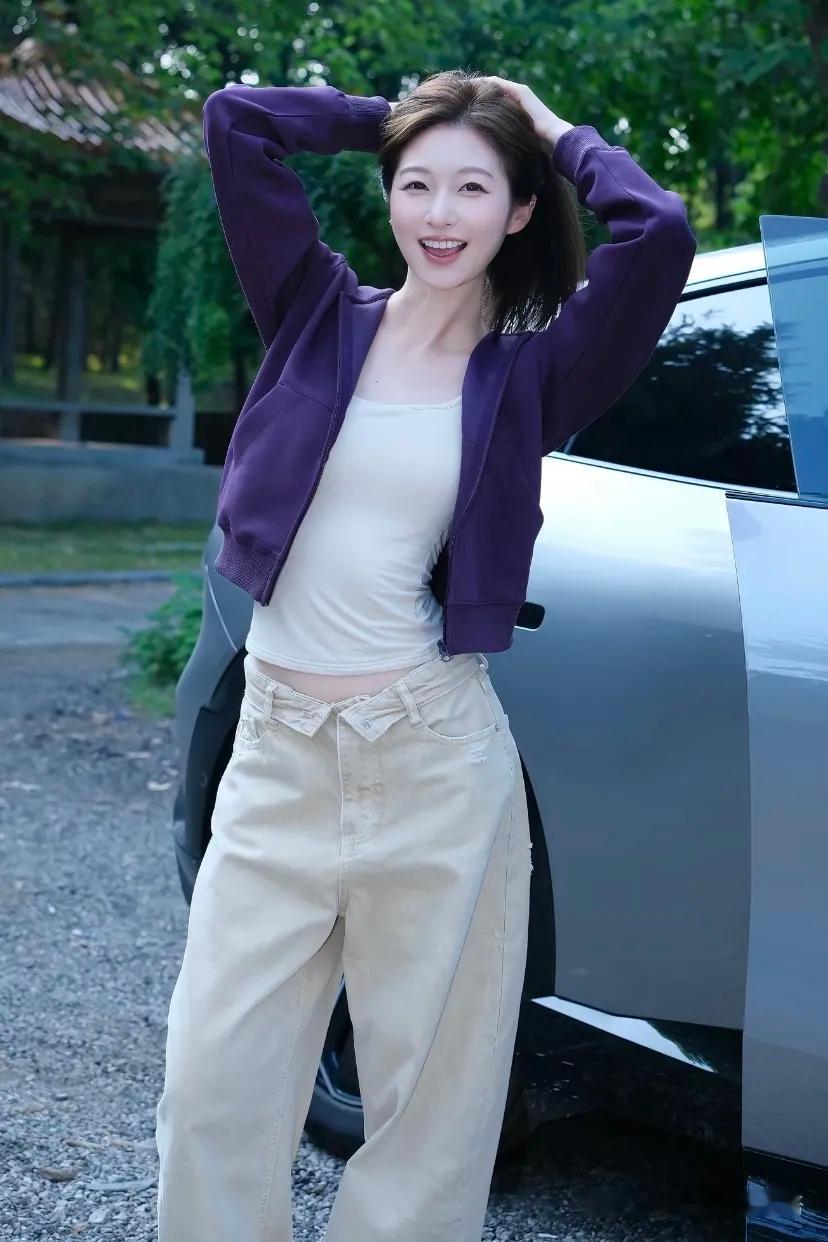 穿紫色外套的女孩在车旁微笑。