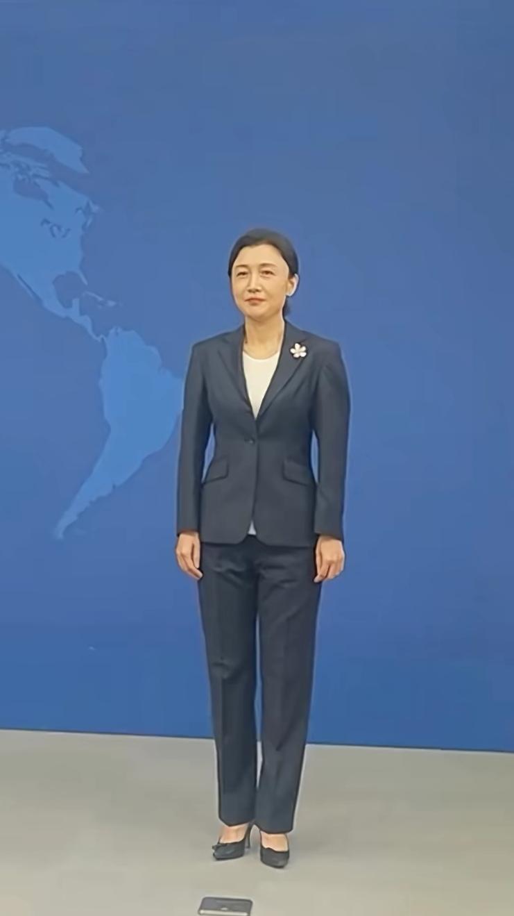 这位女士穿着西装，站在世界地图前。