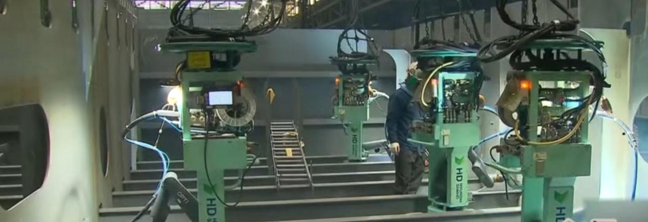 现代重工车间里，人机协同勾勒工业新图景。绿色焊接机器人精准舞动机械臂，在焊花弧光