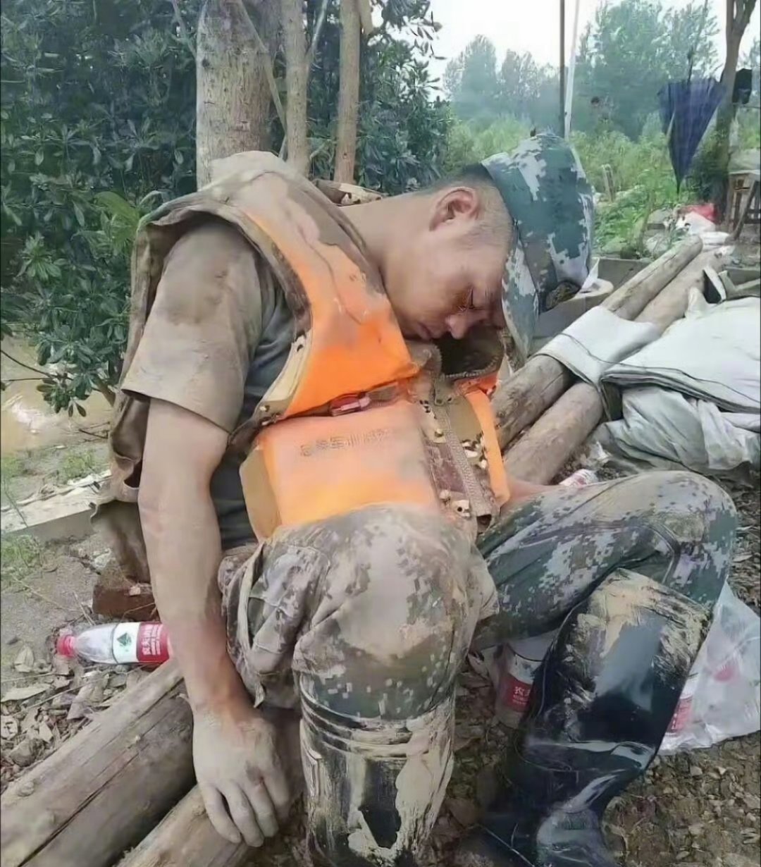 刷到这张照片真的破防了——一个浑身泥浆的兵哥哥，靠树睡着了，橙色救生衣都没脱。又