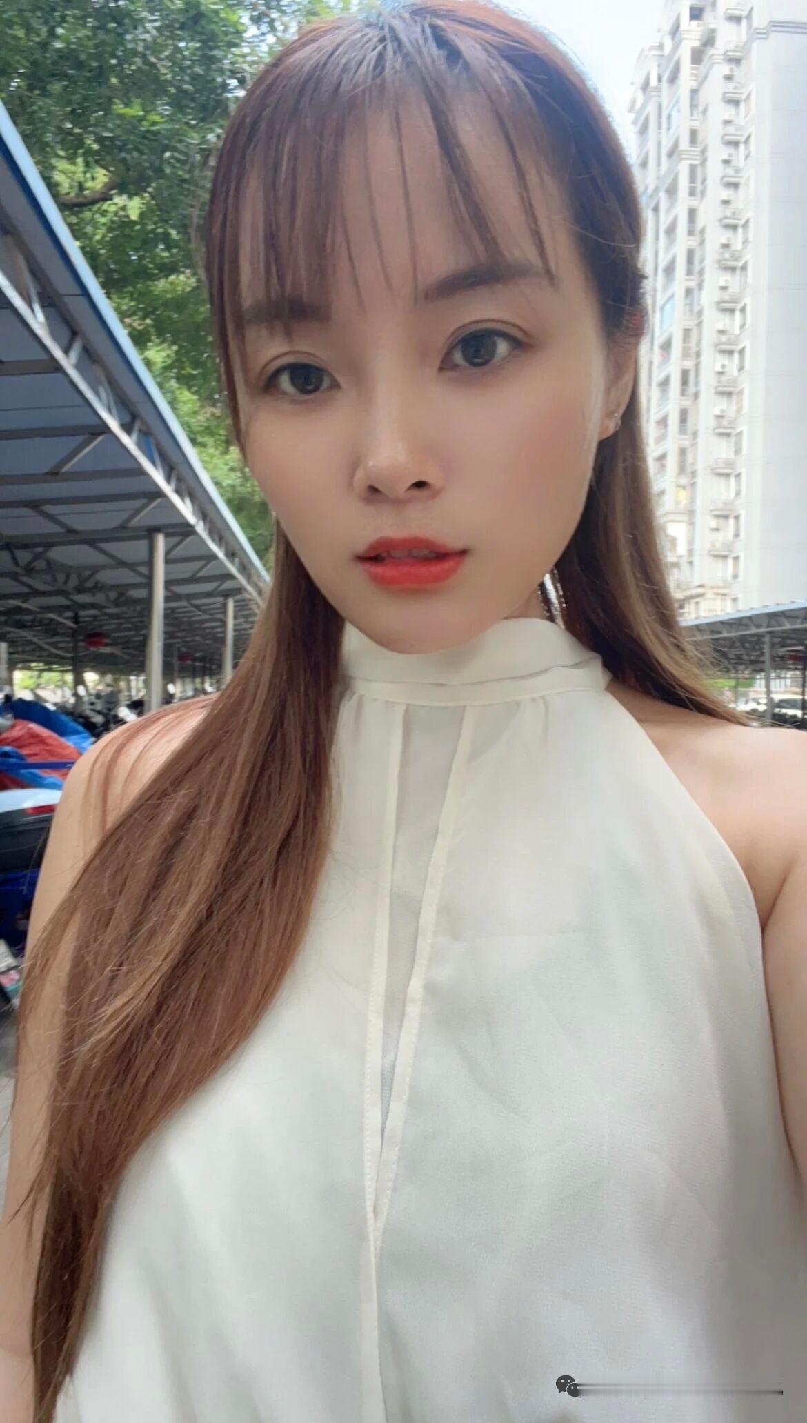 这位美女在户外自拍，背景有建筑和绿树。