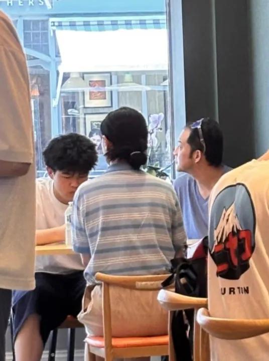 沙溢一家伦敦被偶遇，
胡可穿着蓝色条纹T恤，
面朝窗外坐着，
发髻低挽，
松弛休
