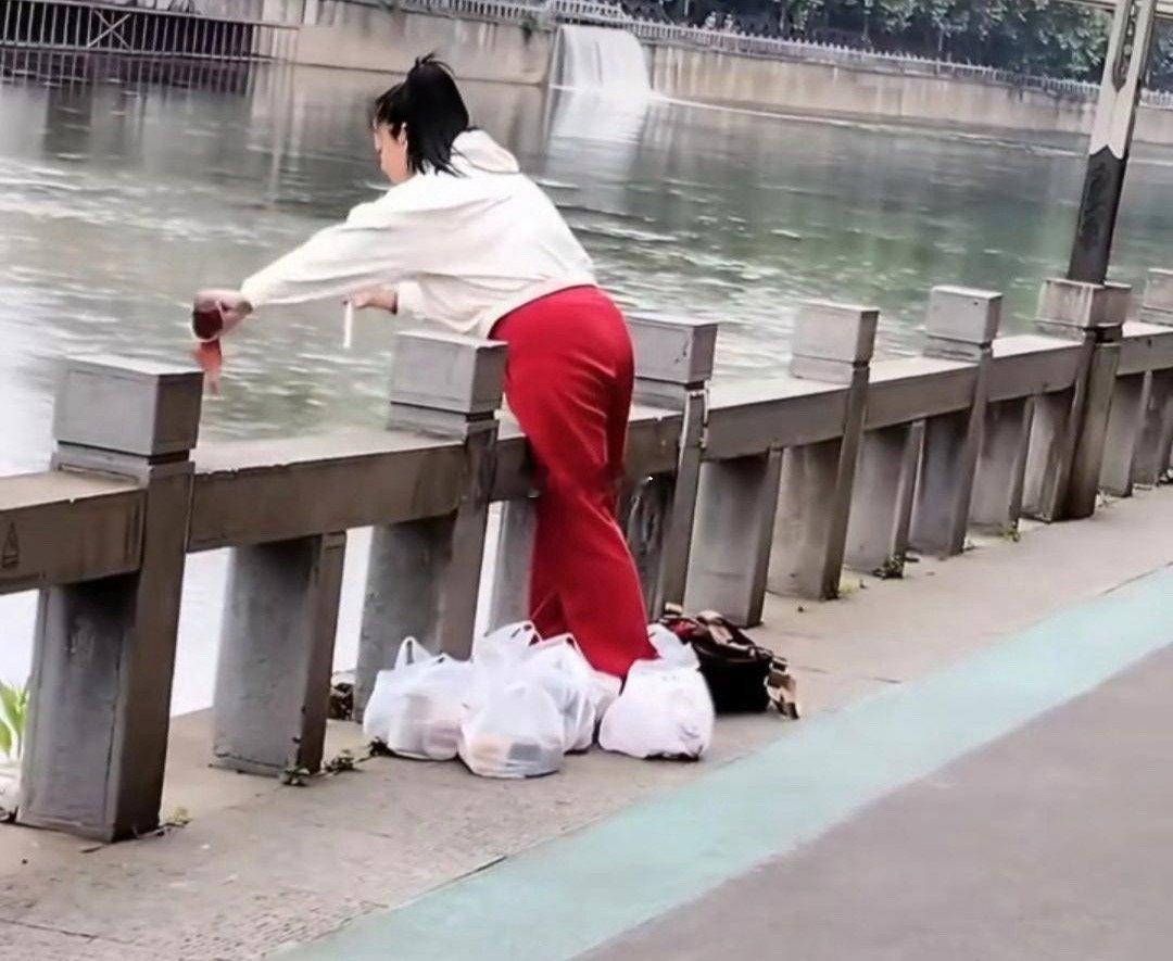 女子带着几袋子的饮品往河里倒 是什么操作？有人说她是在“放生” 因为听到女子嘴里