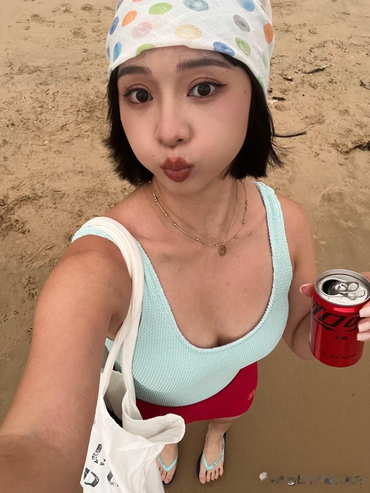 薄荷绿背心配红裙，加上那个彩色波点头巾，色彩搭配在海边特别亮眼。手里拿着饮料（红