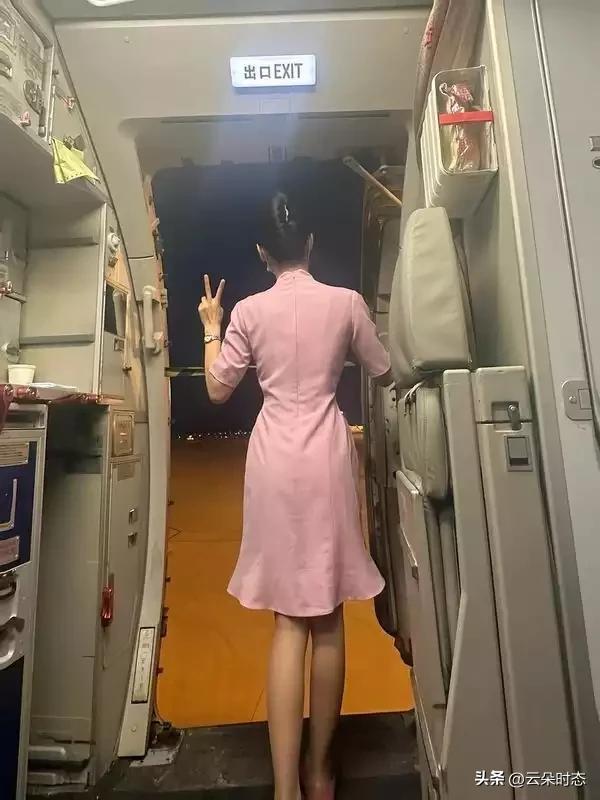 机舱口的暖黄灯光晕开一层柔波，粉色裙裾顺着脊背的曲线轻轻收拢，将腰肢的纤细线条衬