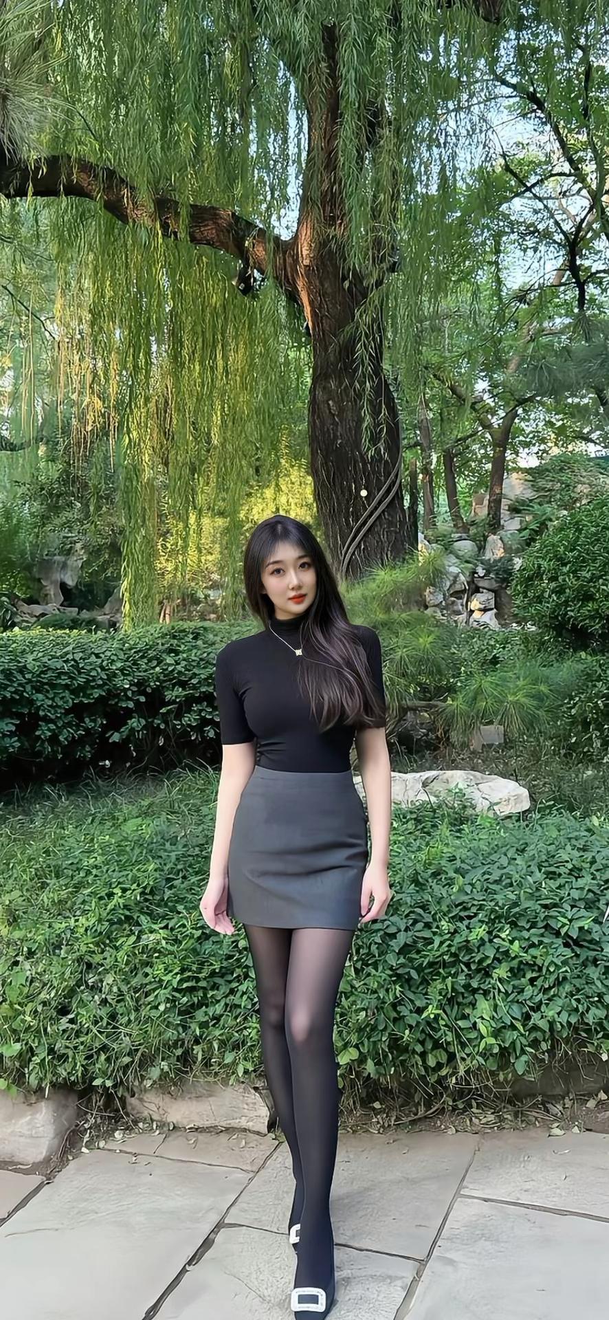 乌黑的长卷发自然垂落，妆容精致，红唇点缀，气质清冷又迷人。背景是绿意盎然的园林，