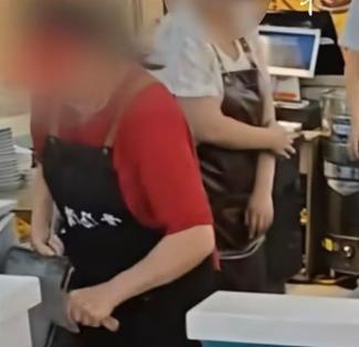 一家餐饮门店里，一名穿着工服、系着围裙的店员，手里握着店里切菜用的菜刀，直接拿刀