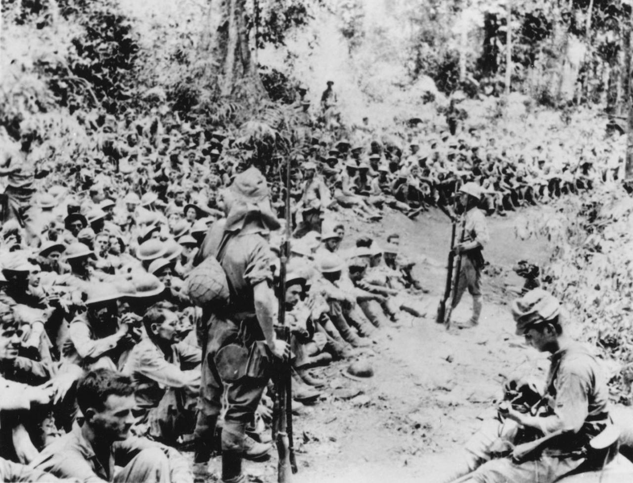 1942年4月，菲律宾巴丹半岛，几名日军士兵看守着一群被俘的美军士兵。