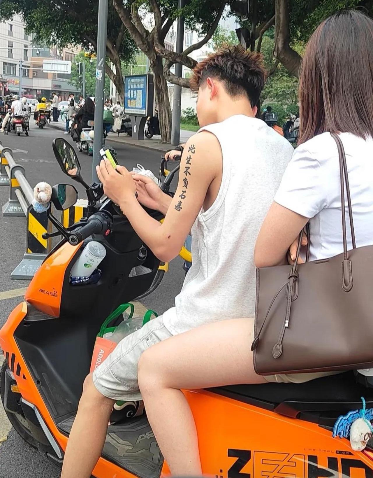 小伙胳膊上纹着此生不负石嘉，后座载着女朋友，一边骑车一边低头玩手机。
不知道石嘉