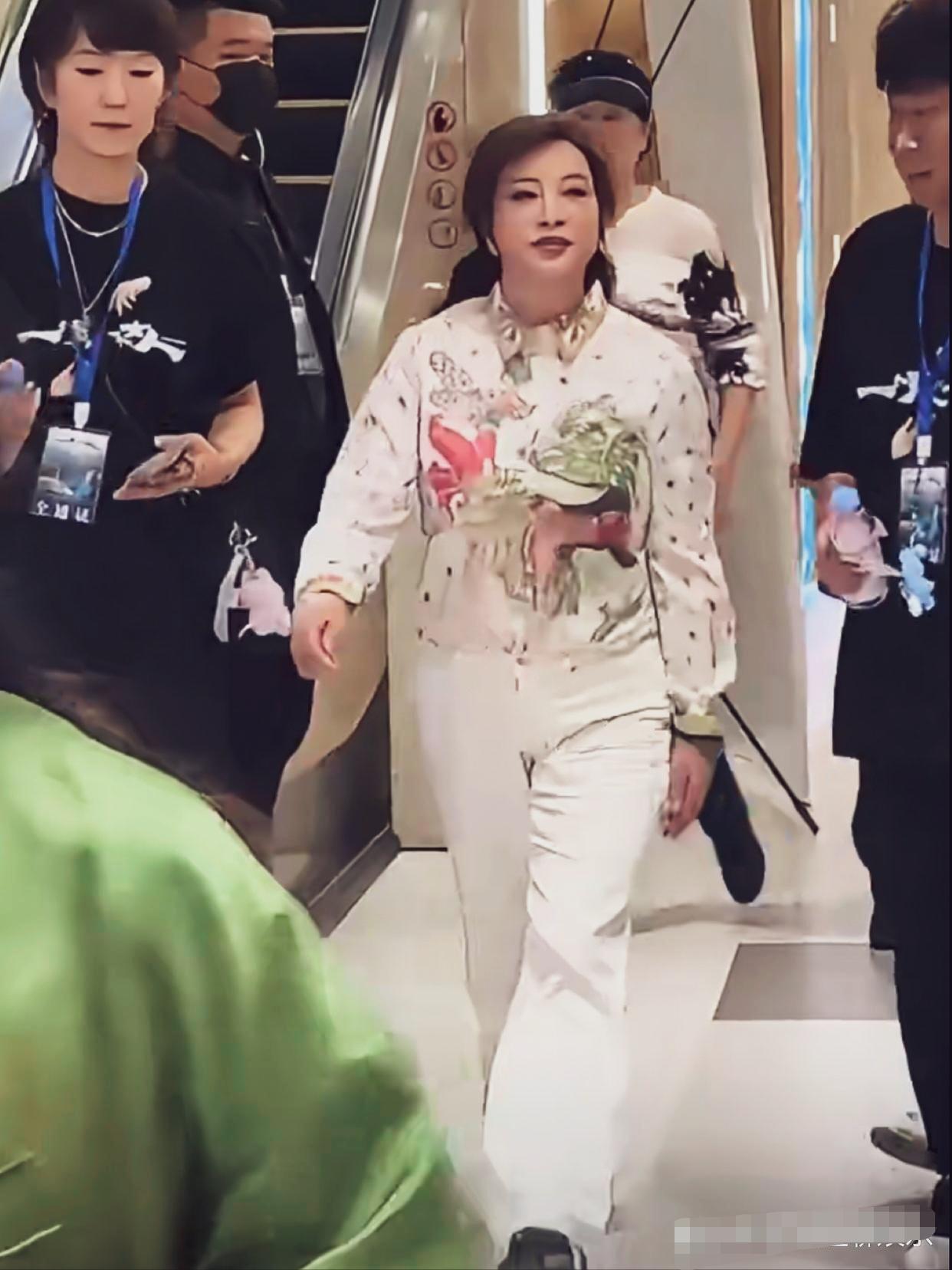 刘晓庆白底印花翻领长袖花衬衫，纯白色直筒休闲长裤，身材臃肿，但走起路来精神抖擞步