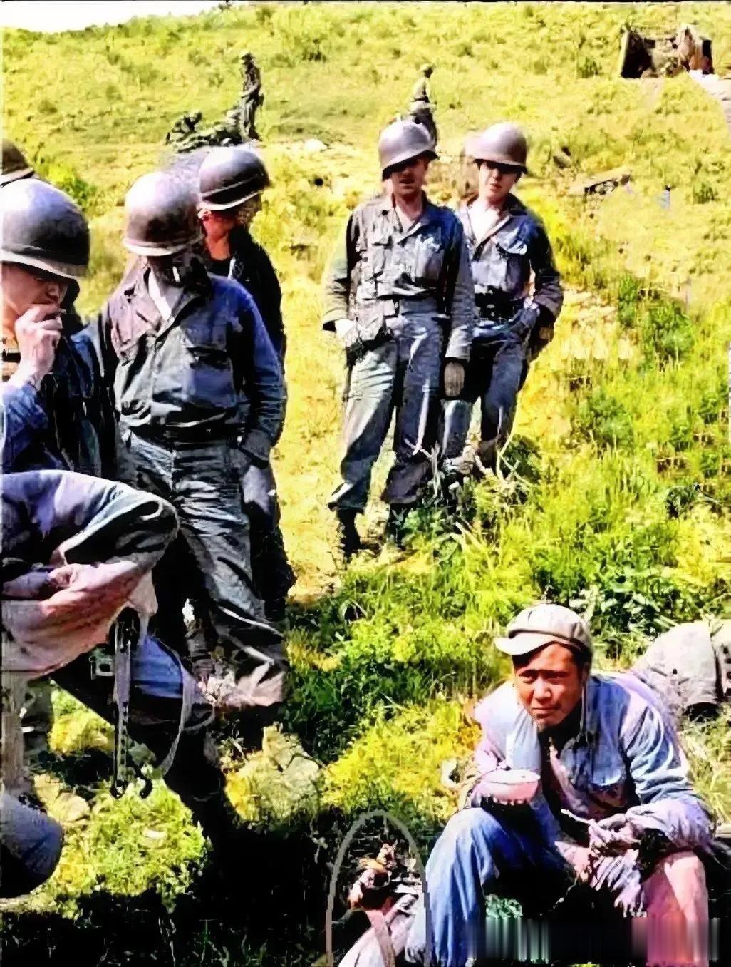 抗美援朝时期，一名不幸被俘虏的志愿军战士坐在地上，周围都是虎视眈眈的看着他的美军