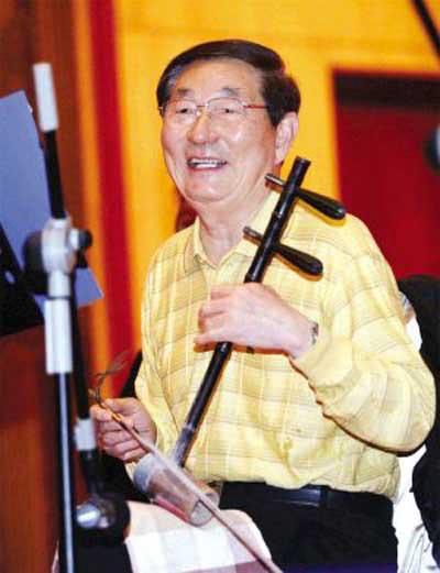 这张照片记录的是朱镕基持京胡准备演奏的一幕。他一身浅黄色格纹休闲上衣，神情舒展、