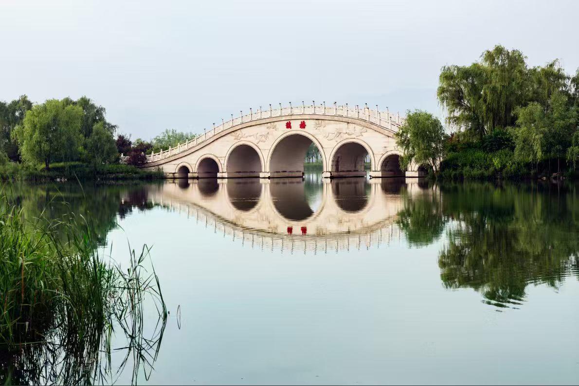 旅行随手拍湖面澄澈如镜，七孔石桥静卧水上，桥身与倒影拼成完整圆影，两岸垂柳依依、