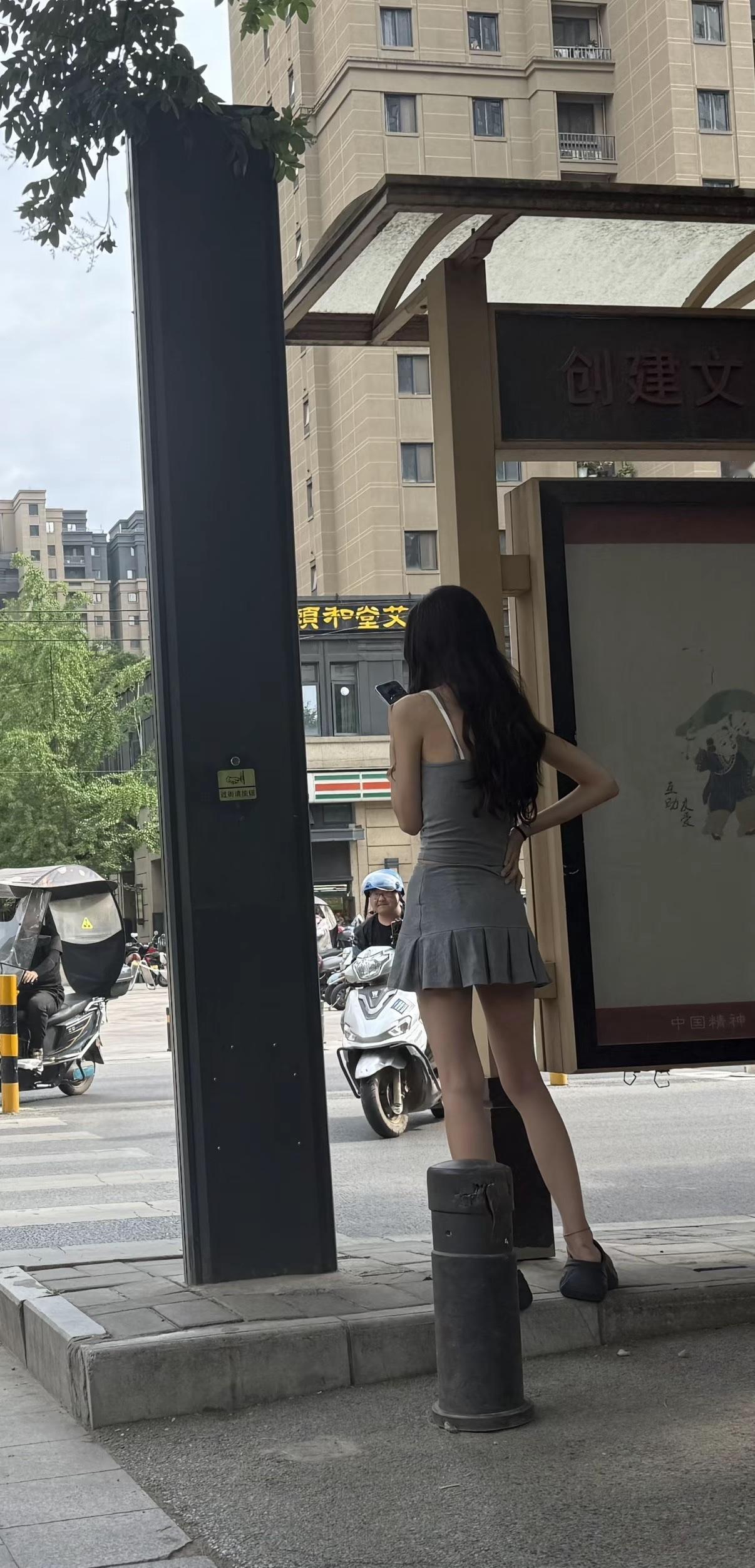 都市街头，时尚女孩倚靠公交站牌，等待中尽显优雅。怎么样的穿搭才够时尚 牛仔服配啥