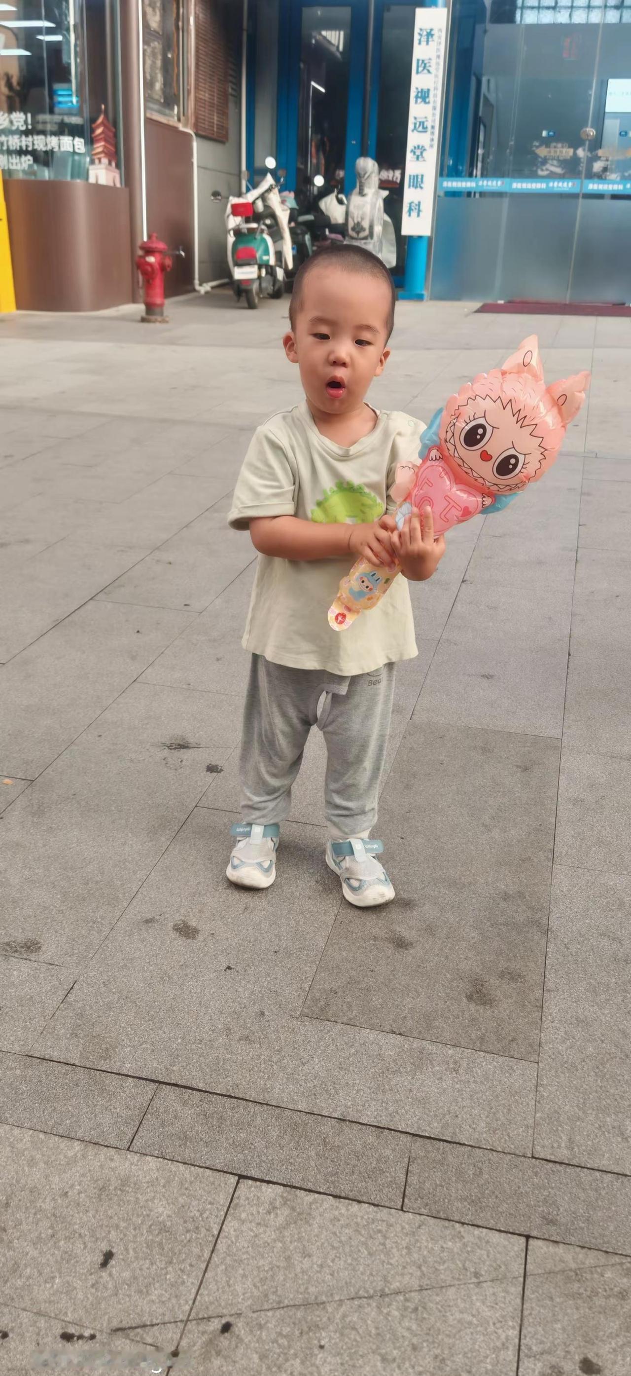 在这片热闹的街头，一个小小的身影手捧着玩偶，仿佛拥有了全世界的柔软与快乐。周围的