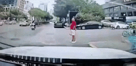 红衣男子挺胸瘪肚的站在汽车面前，任汽车狂按喇叭而置之不理。
视频车要右转弯，而一