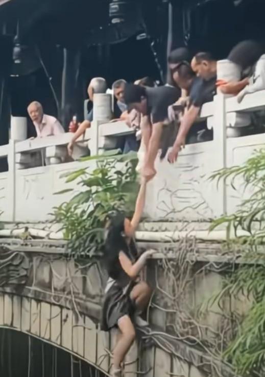 夏日景区一女子悬挂在桥梁外侧，游客上前搭救，
最后还是落入水中，
游客有的把绳子
