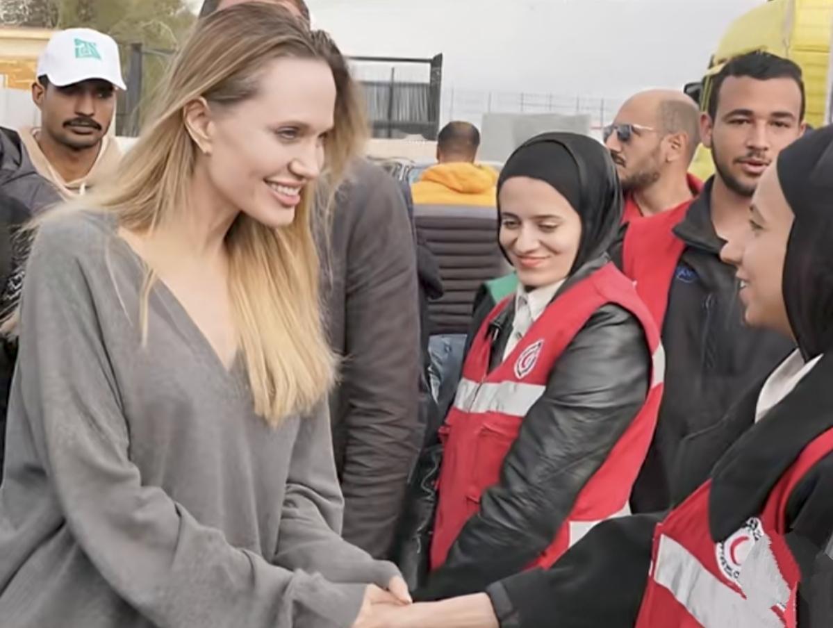 拉法口岸的尘土粘在她的睫毛上。
没有红毯，没有闪光灯。
只有硝烟味和远处隐约的轰