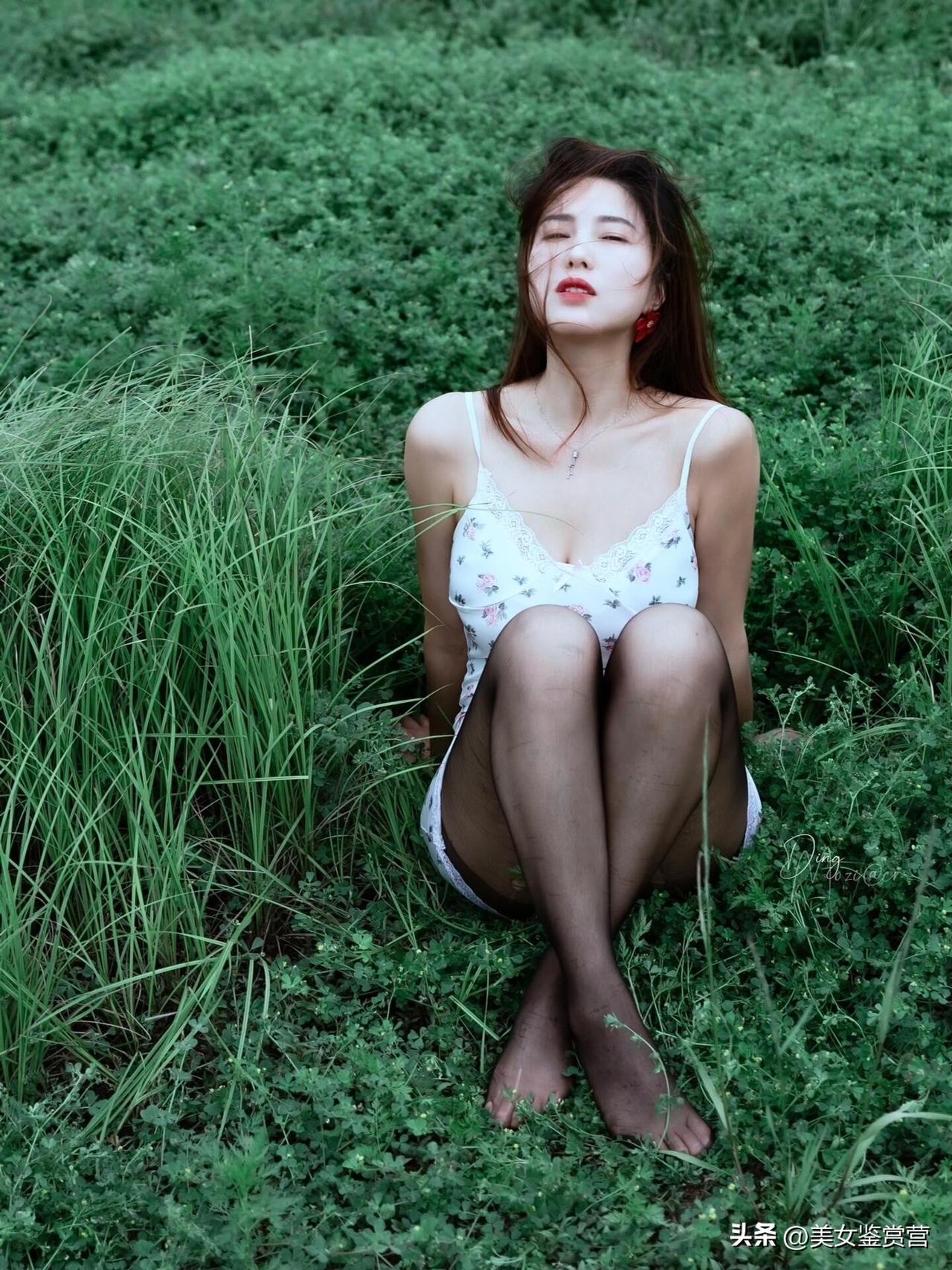 她坐在一片浓绿的草地上，一身白色碎花吊带裙与周围的绿意形成了清新的呼应。
细带与