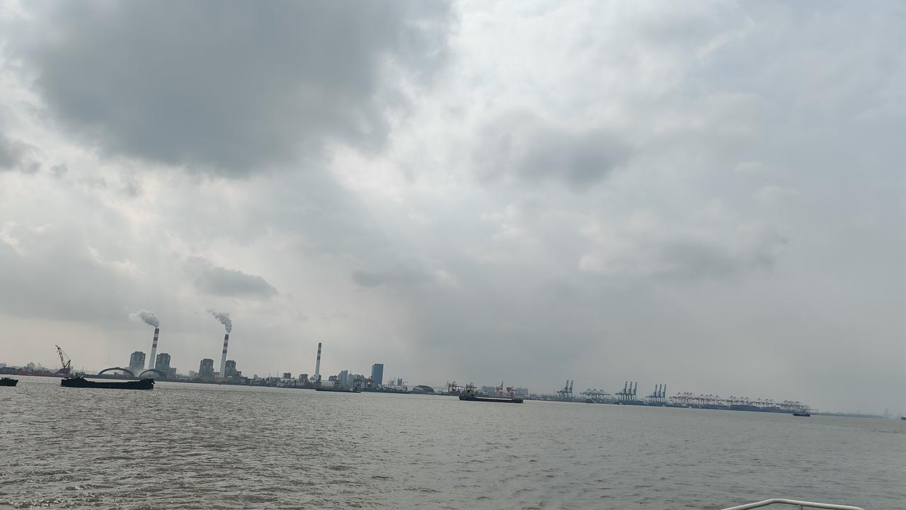 随手发一张海边的照片在黄浦江边，云幕低垂，江水浩渺。货轮与港口机械静默伫立，远处
