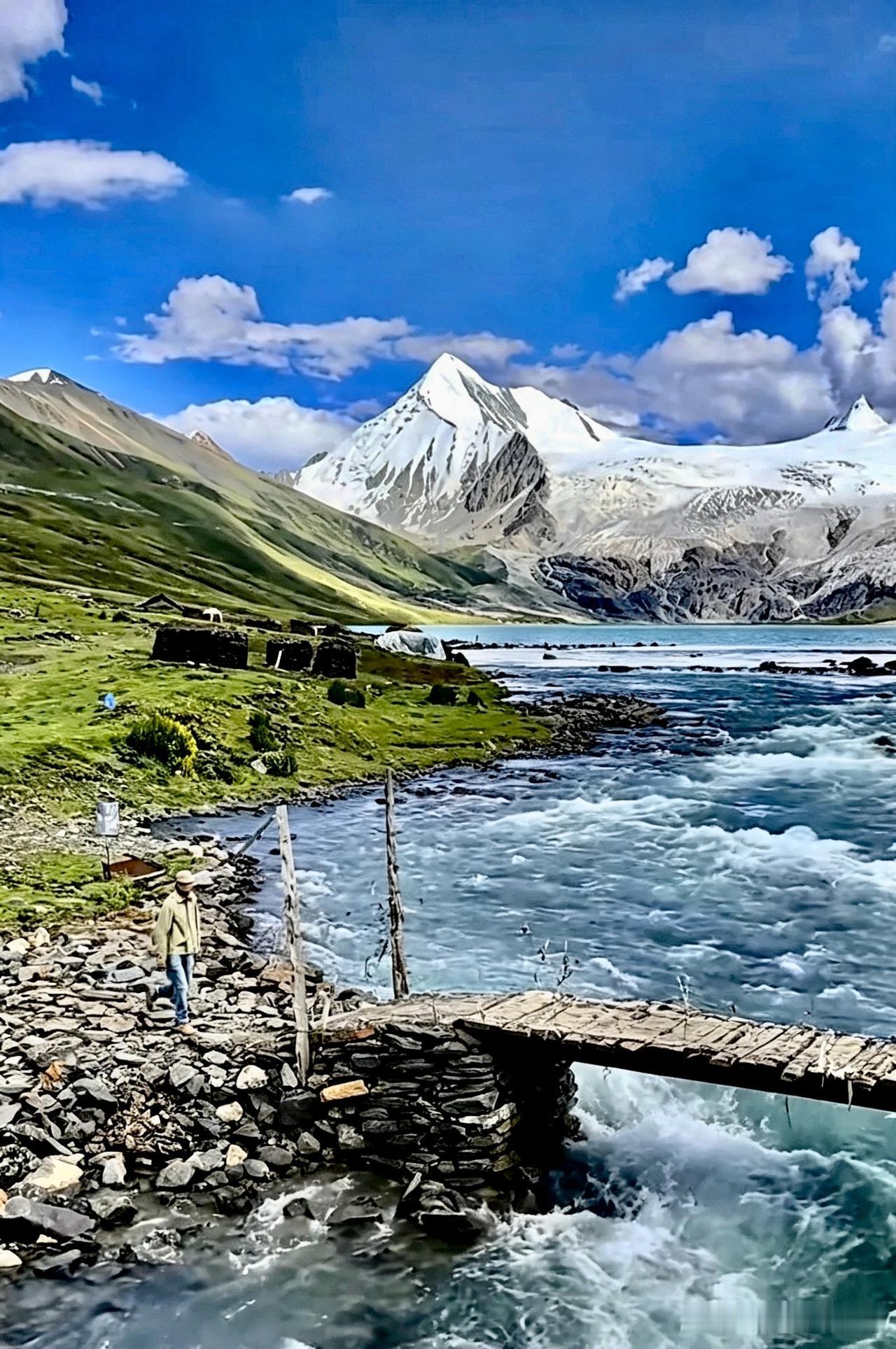 湍急的江水奔涌向前，老旧木桥连通两岸。远处雪峰巍然矗立，青山铺展，置身这片雪域净