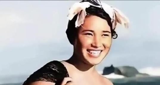 1955年，一名身体强壮的日本女人赤裸上半身，背着一个黑色的编织袋站在海边。这个