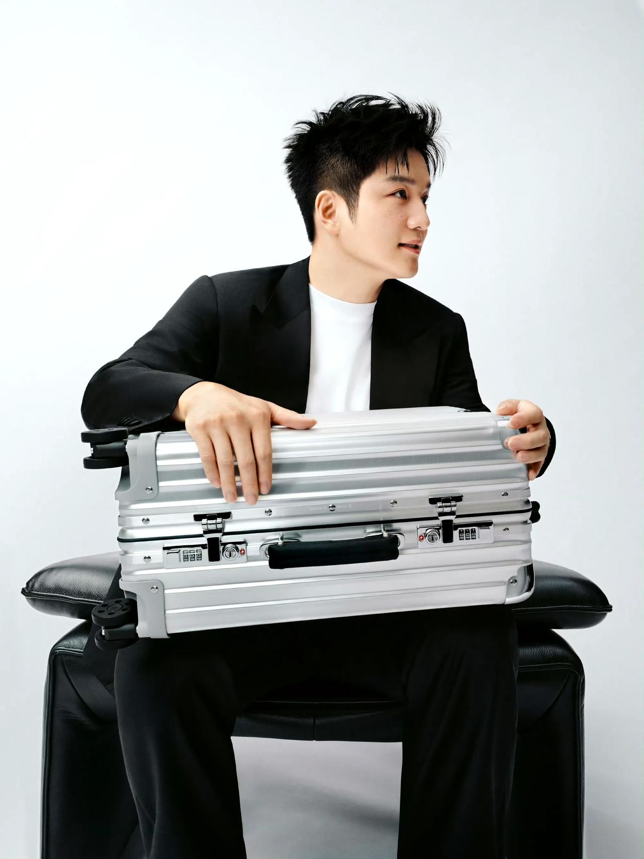 内搭白色体恤，外穿黑色西服！一头黑色时尚新潮的发型。手拿白色亮闪闪的行李箱。这侧