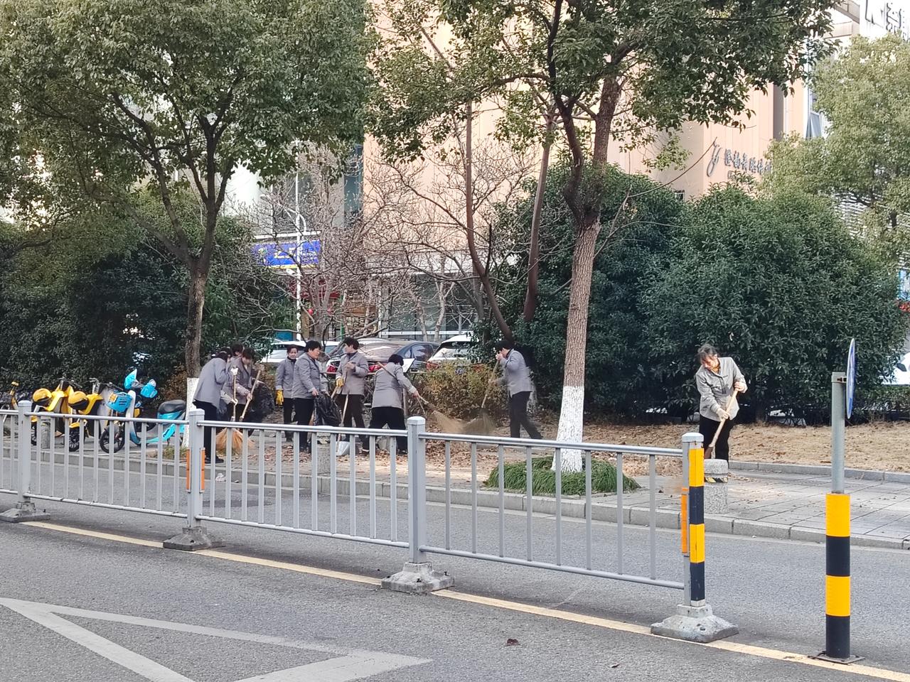 在楼下遇见10位物业保洁员，他们正在清理道路上的落叶。有的使用竹制扫把，有的手拿