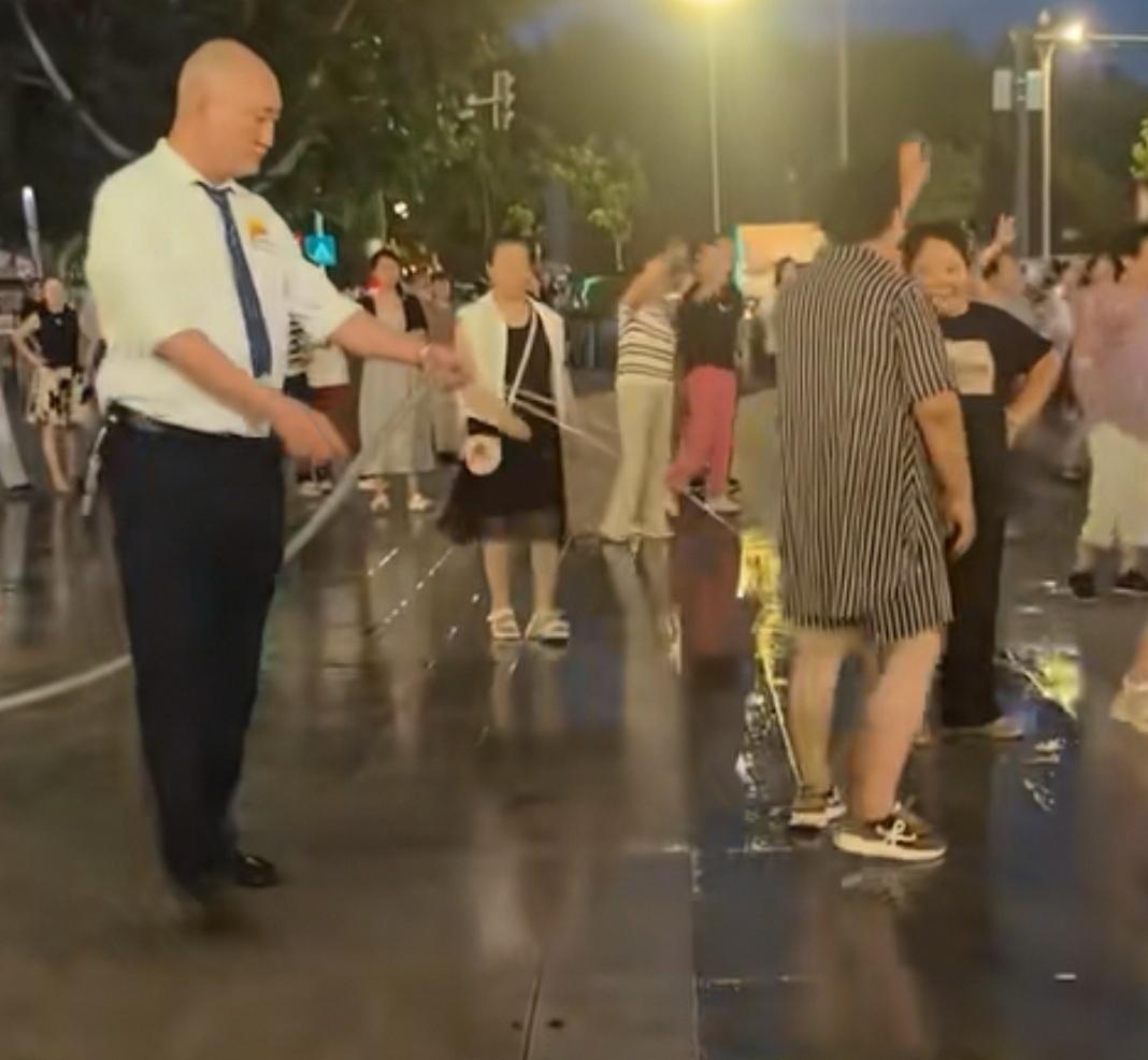 6月30日，陕西西安，某商场门口，一群大妈在跳广场舞。商场工作人员一边用水管洒水