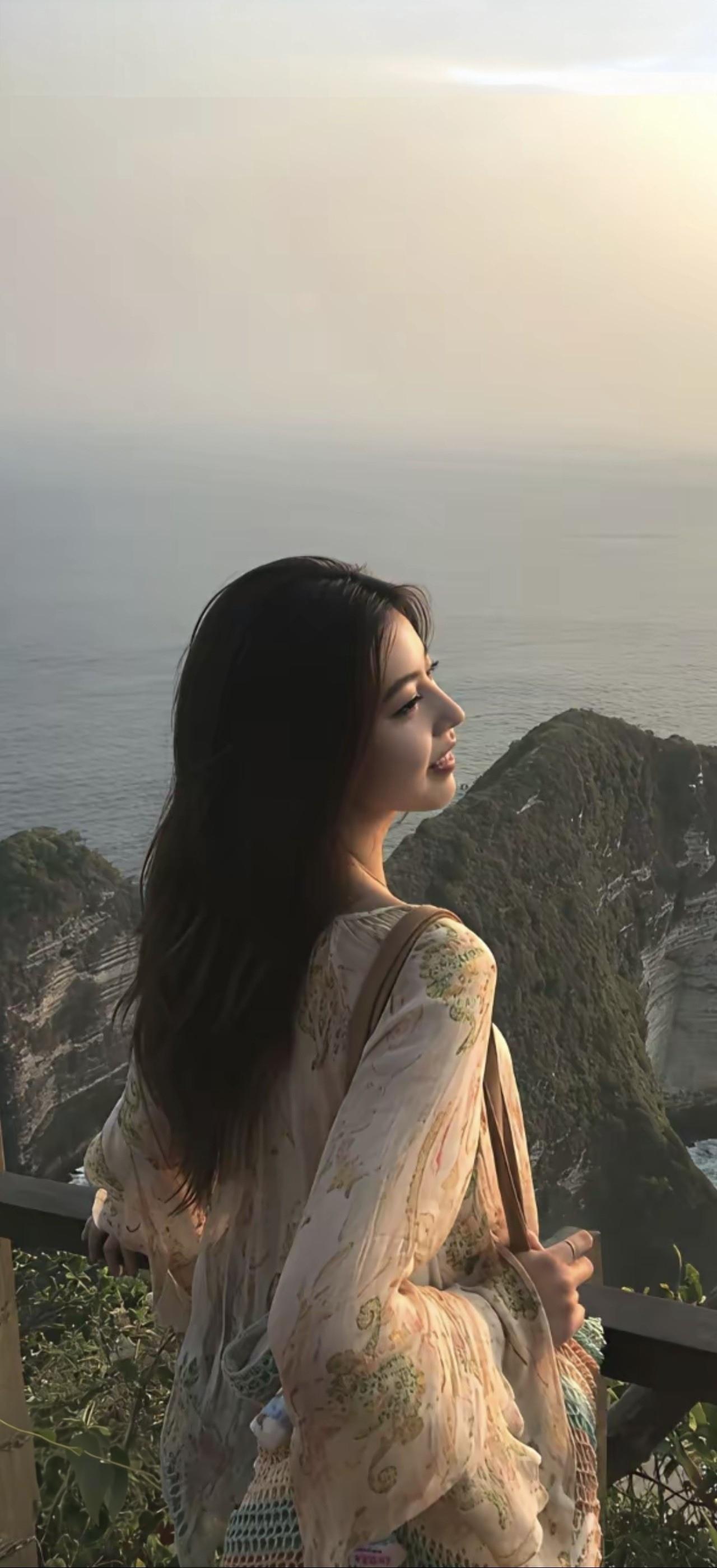女孩站在海边，欣赏美丽风景。