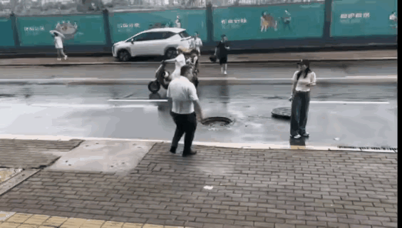 马路上，一个马葫芦井盖掀翻到一旁，路上车水马龙，很多人都熟视无睹。
可是一个戴着